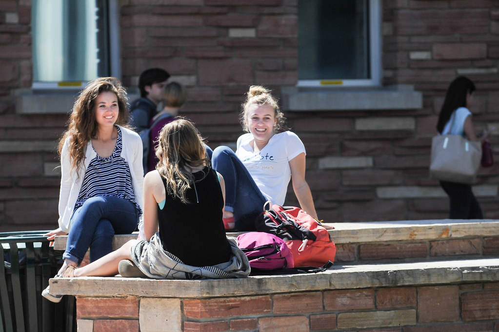 Students sit and talk sitting outside on a low stone wall