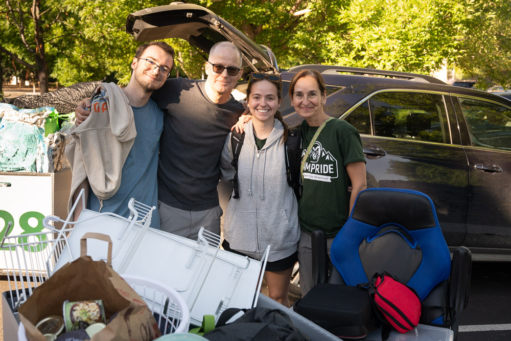 First year student stands with family and move-in supplies