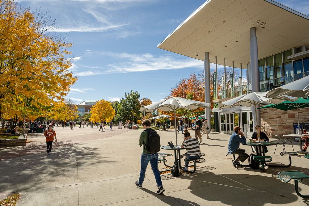 Student walks by the Lory Student Center with fall trees around it